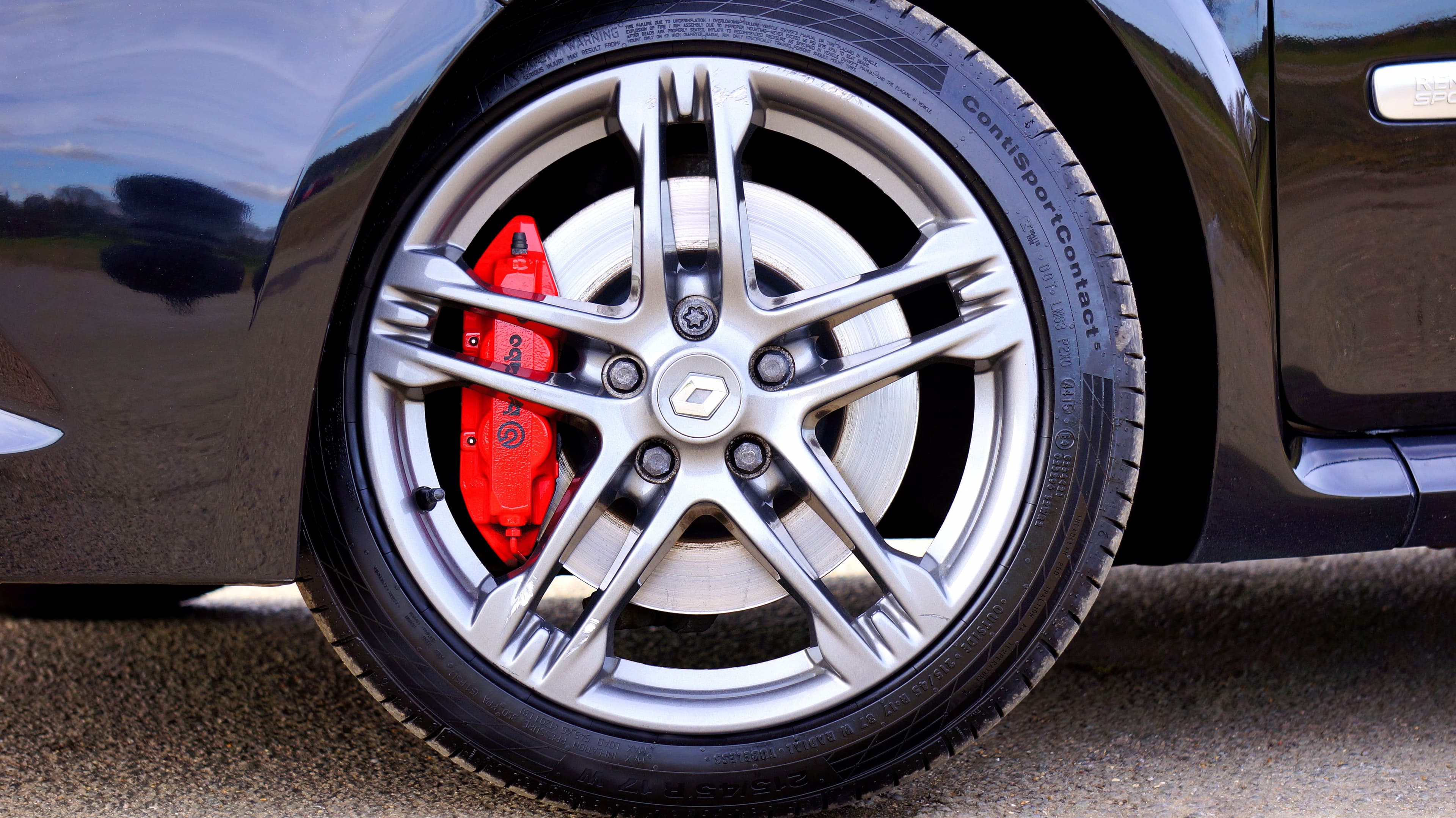 Close up of a car brake disc and caliper behind an alloy wheel